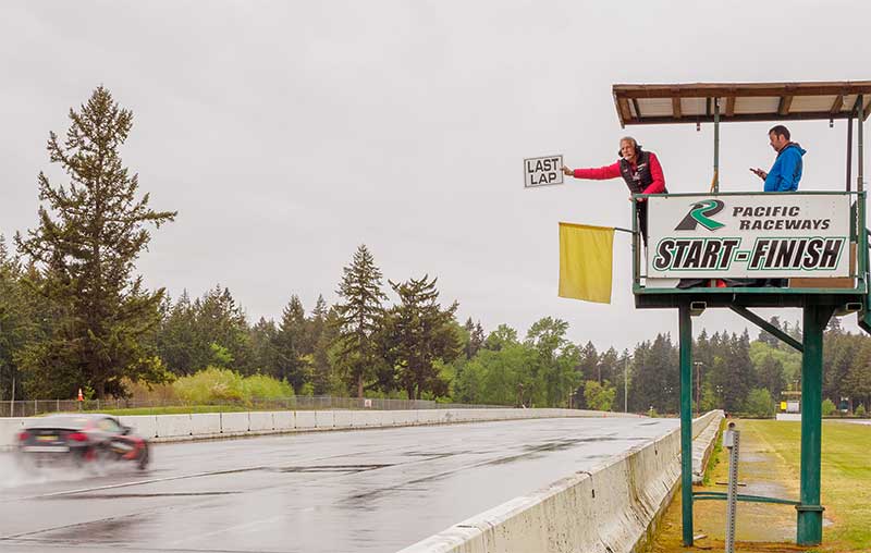 flag marshal holding out "last lap" sign as car races by on racetrack