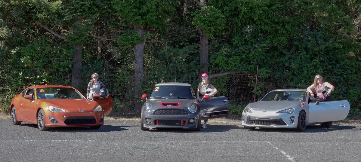 Three sports cars with women standing by them holding helmets